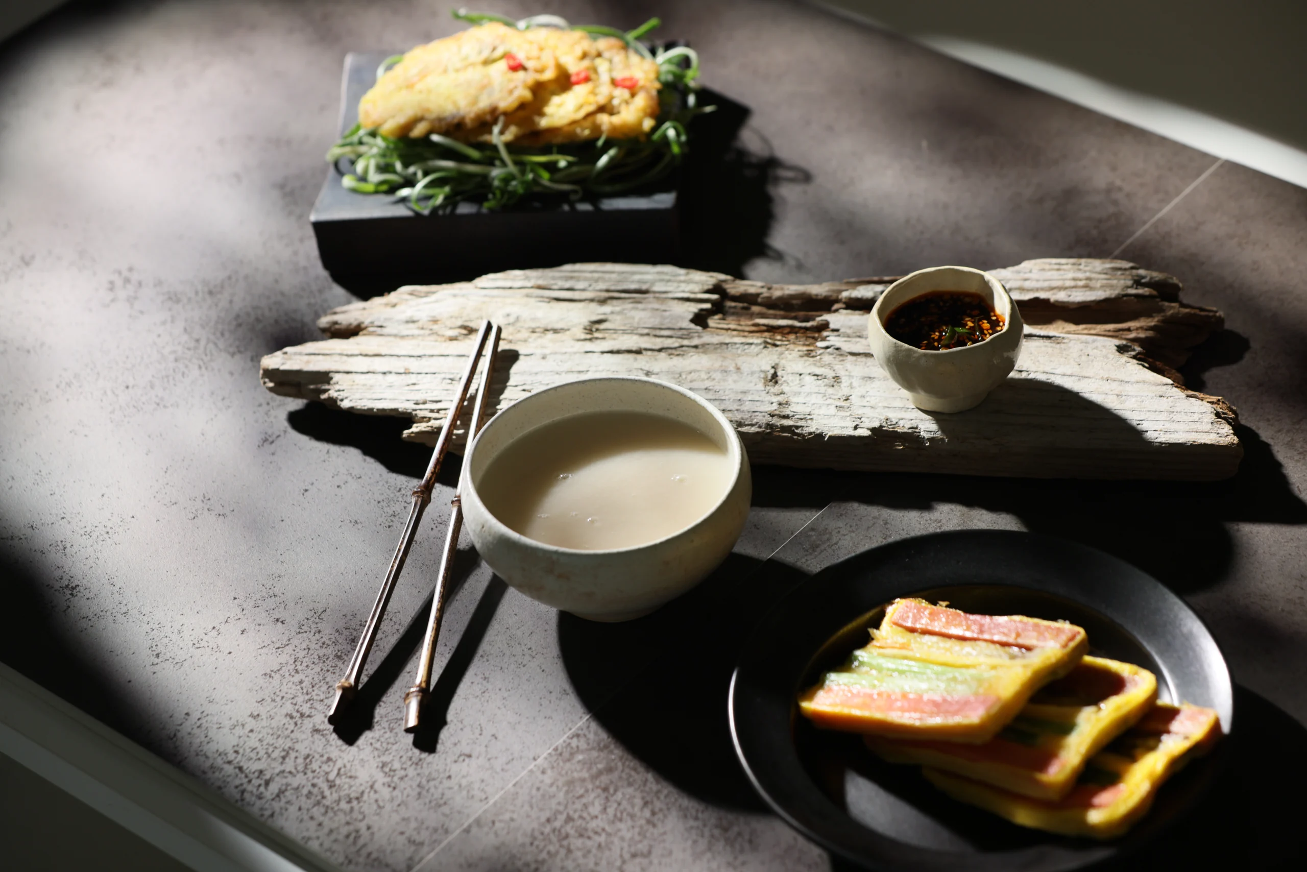 Makgeolli được phục vụ trong một bát gốm bên cạnh đồ ăn Hàn Quốc